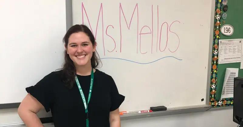 Ana Melos stands in front of a whiteboard, which reads "Ms. Mellos."